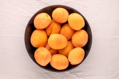 Siyah seramik bir tabakta, keten bir kumaş, makro, üst manzara üzerinde birkaç olgun sulu kayısı..