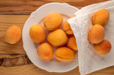 Beyaz seramik tabakta, ahşap bir masada, makroda, üst manzarada bir sürü sulu kayısı..