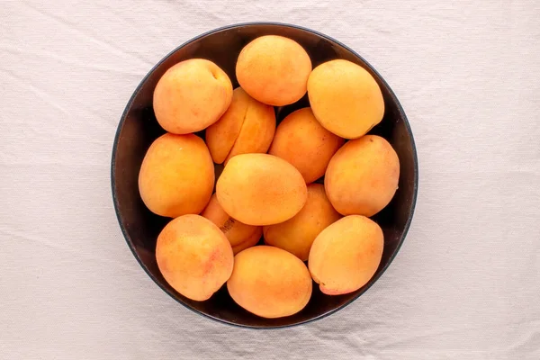 Siyah seramik bir tabakta, keten bir kumaş, makro, üst manzara üzerinde birkaç olgun sulu kayısı..