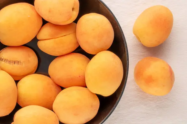 Siyah seramik bir tabakta, keten bir kumaş, makro, üst manzara üzerinde birkaç olgun sulu kayısı..