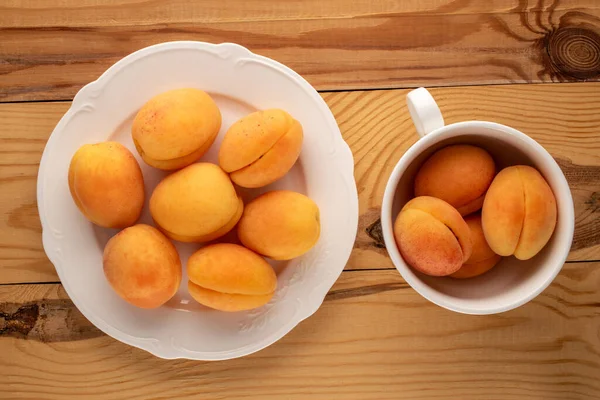 Beyaz seramik bir tabakta bir kaç sulu kayısı ve tahta bir masada bir fincan, makro, üst manzara..