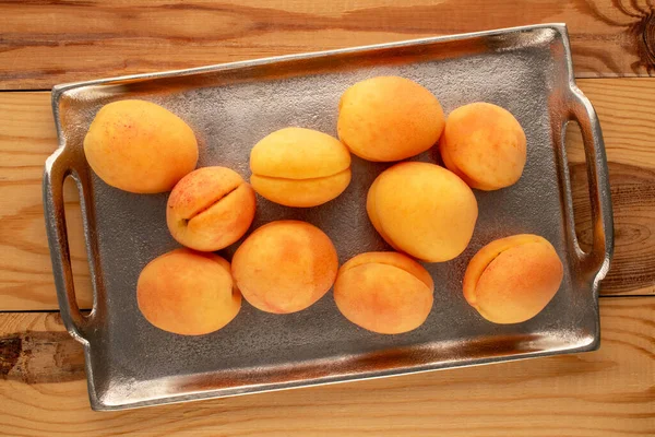 Tahta bir masanın üzerinde metal tepsi ve makro manzaralı birkaç sarı sulu kayısı..