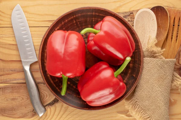 stock image Three sweet red peppers with ceramic plate, knife and wooden spoons, macro, top view.