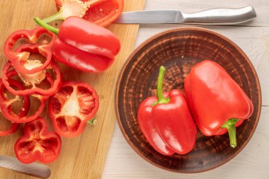 Bir sürü kırmızı biber, kil levha ve bıçakla dilimlenmiş. Tahta masa, makro, üst manzara..