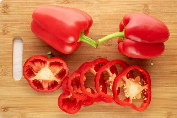 Two Red Peppers Whole Sliced Bamboo Kitchen Board Macro Top — Stock Photo, Image