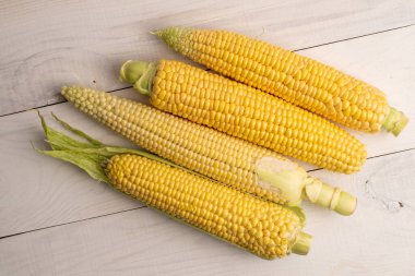 Dört tatlı organik mısır koçanı, yakın plan, beyaz ahşap masa, üst manzara.