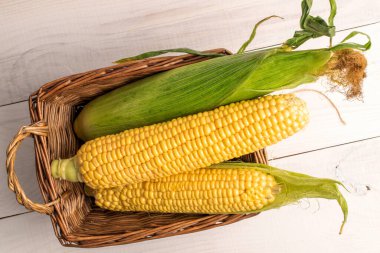 Hasır sepetin içinde üç mısır koçanı, yakın plan, beyaz ahşap masa, üst görüş..