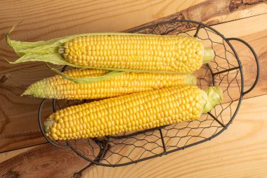 Üç mısır koçanı metal bir sepetin içinde, yakın planda, ahşap bir masanın üstünde, üst tarafta..