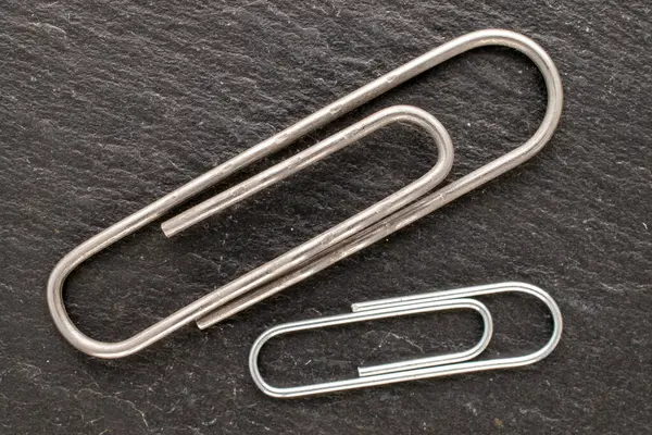 Two metal paper clips on slate stone, macro, top view.