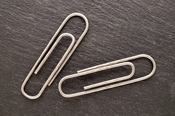 Two metal paper clips on slate stone, macro, top view.