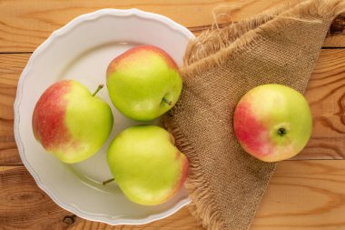 Beyaz seramik plakalı birkaç yeşil elma, ahşap masada jüt peçete, makro, üst manzara..