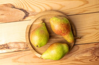 Yuvarlak bir ahşap tepside üç olgun armut, yakın plan, ahşap masa, üst görüş..