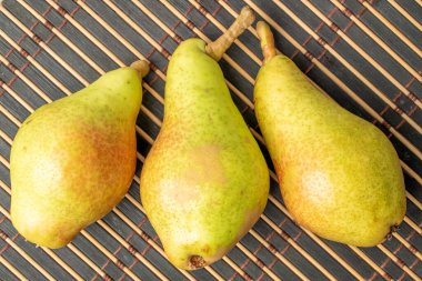 Üç olgun armut, yakın çekim, bambu bir hasırın üzerinde, üst manzara..