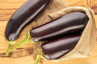 Üç olgun patlıcan ve tahta bir masanın üstünde jüt çanta, makro, üst manzara..