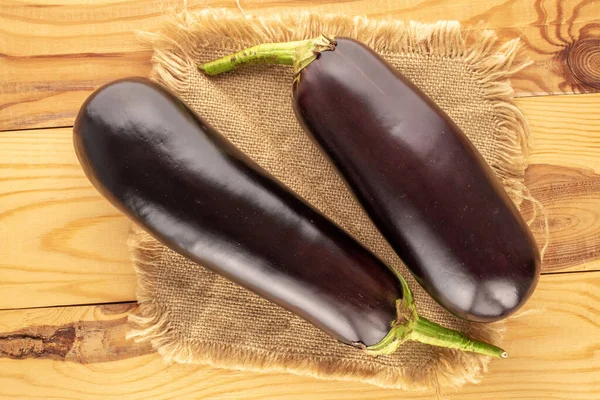 Two ripe eggplants with a jute napkin on a wooden table, macro, top view.
