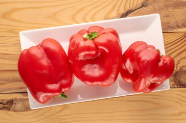 Tahta masada beyaz seramik plakalı üç tatlı kırmızı biber, makro, üst manzara..
