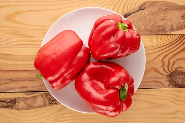 Tahta masada beyaz seramik plakalı üç tatlı kırmızı biber, makro, üst manzara..