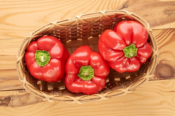 Three sweet red peppers in a basket on a wooden table, macro, top view.