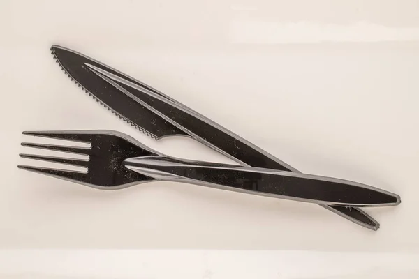 One plastic knife and fork on a white ceramic plate, macro, top view.