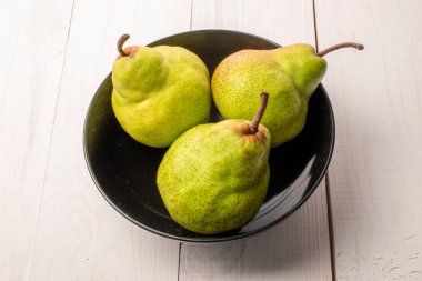 Siyah seramik tabaklı üç tatlı armut, yakın plan, ahşap bir masanın üzerinde..