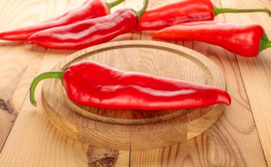 Ahşap bir masanın üzerinde ahşap tepsiyle bir sürü kırmızı biber.