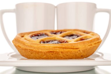 İki fincanlı, seramik tabakta reçelli bir kurabiye, makro, beyaz arka planda izole edilmiş..