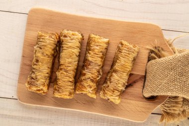 Tahta bir masa üzerinde ahşap bir mutfak tahtası ve makro manzaralı birkaç parça tatlı baklava..