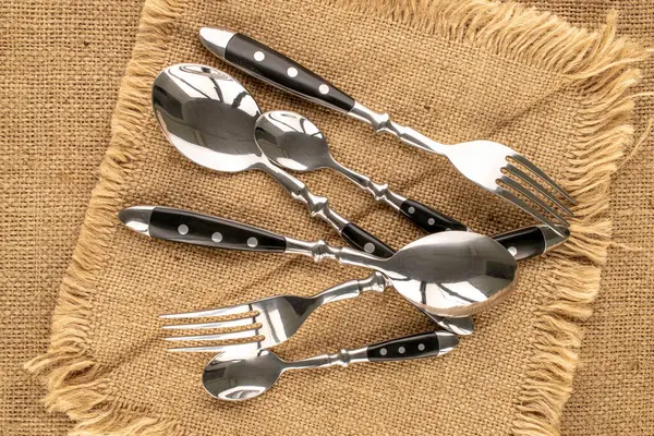Several metal spoons and forks on a jute napkin, macro, top view.
