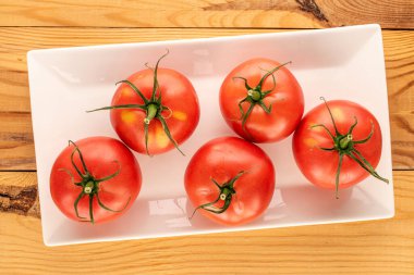 Tahta bir masanın üzerinde beyaz seramik plakalı, olgun kırmızı domatesler..