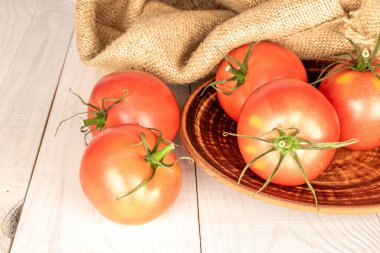 Tahta bir masanın üzerinde kilden bir plaka ile olgunlaşmış birkaç kırmızı domates, makro.