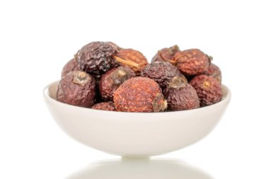 Beyaz bir seramik tabakta, makroda, beyaz arka planda izole edilmiş birkaç kuru gül çileği..