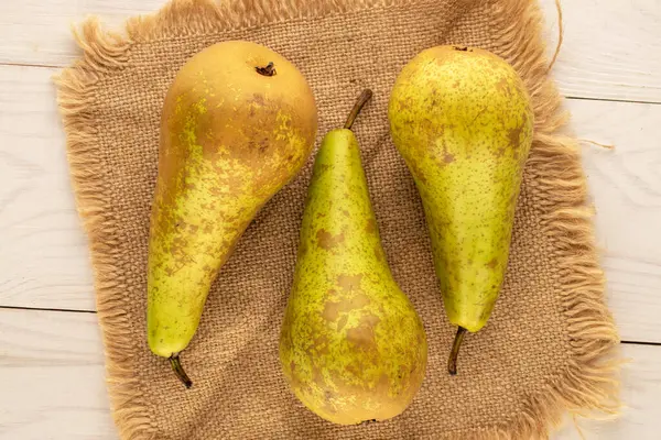 Three ripe pears with a jute napkin on a wooden table, macro, top view.