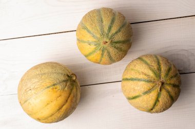 Üç güzel kokulu organik kavun, yakın plan, beyaz ahşap masa, üst manzara.