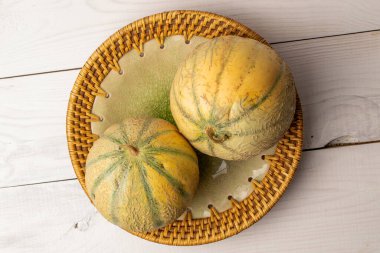 Seramik bir tabakta iki güzel kokulu organik kavun, yakın plan, beyaz ahşap masa, üst görüş..