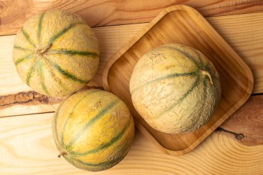 Üç güzel kokulu organik kavun, bambu tepsiyle, yakın planda, ahşap bir masada, üst tarafta..