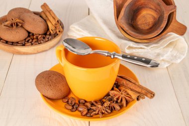 Çikolatalı kurabiyeler, tarçın, yıldız anason, seramik tabakta kahve çekirdekleri, ahşap bir masada bir fincan..