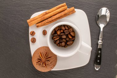 Çikolatalı kurabiye, tarçın, yıldız anason ve kahve çekirdekleri seramik bardak ve çay tabağı ile kayrak taşı, makro, üst görünüm.