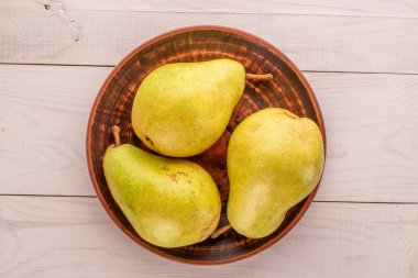 Üç organik olgun armut, ahşap masa üzerinde kil plaka, makro, üst manzara.