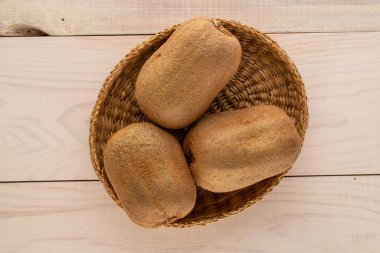 Tahta bir masa, makro, üst görünüm üzerinde saman bir tabakta üç olgun kivi.