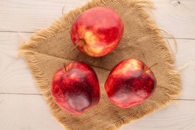 Üç kırmızı organik elma jüt peçete ile ahşap masa, makro, üst görünüm.