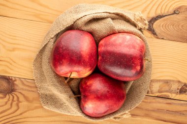 Üç kırmızı organik elma bir jüt torba içinde ahşap bir masa, makro, üst manzara.