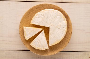 Ahşap bir masanın üstünde seramik tabağı olan mis kokulu Brie peyniri, makro, üst manzara..