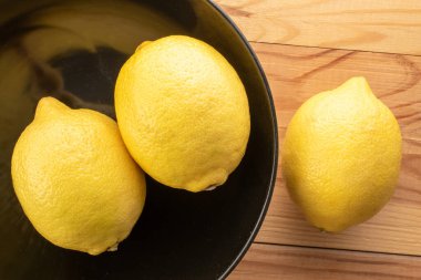 Üç sarı olgun limon siyah seramik bir tabakta, ahşap bir masada, yakın plan, üst manzara..