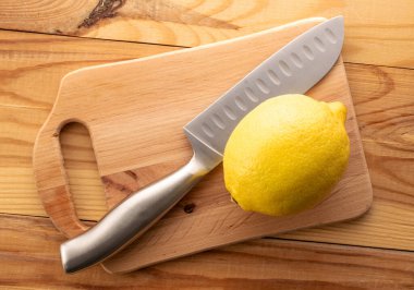 Tahta bir masanın üzerinde metal bir bıçakla sarı olgun bir limon, yakın plan, üst görüş..