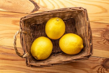 Üç sarı olgun limon, bir sepet sarmaşık, ahşap bir masada, yakın plan, üst manzara..