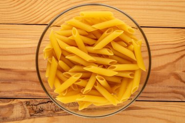 Çiğ makarna, penne, cam tabakta ahşap masa, makro, üst manzara.