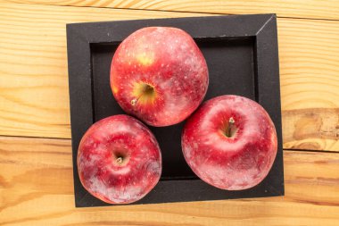 Tahta bir masada ahşap tepside üç kırmızı elma, makro, üst manzara..