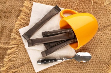 Seramik bardaklı birkaç kağıt şeker, jüt kumaş, makro, üst görünümde kaşık ve çay tabağı..