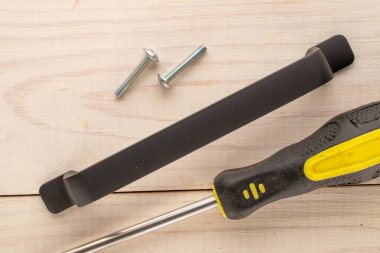 Bir metal çekmece sapı, tornavida ve ahşap masada iki vida..