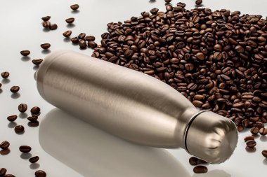 Masada bir metal termos şişesi ve yanında da kavrulmuş kahve çekirdekleri, makro..